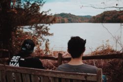 two men sitting on bench looking out onto a lake