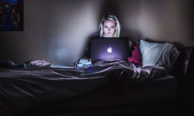 teen in dark room with lit up laptop struggling to sleep